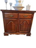 Cherry wood server buffet with two drawers and two arched-panel cabinet doors, brass hardware, shown with decorative items on top
