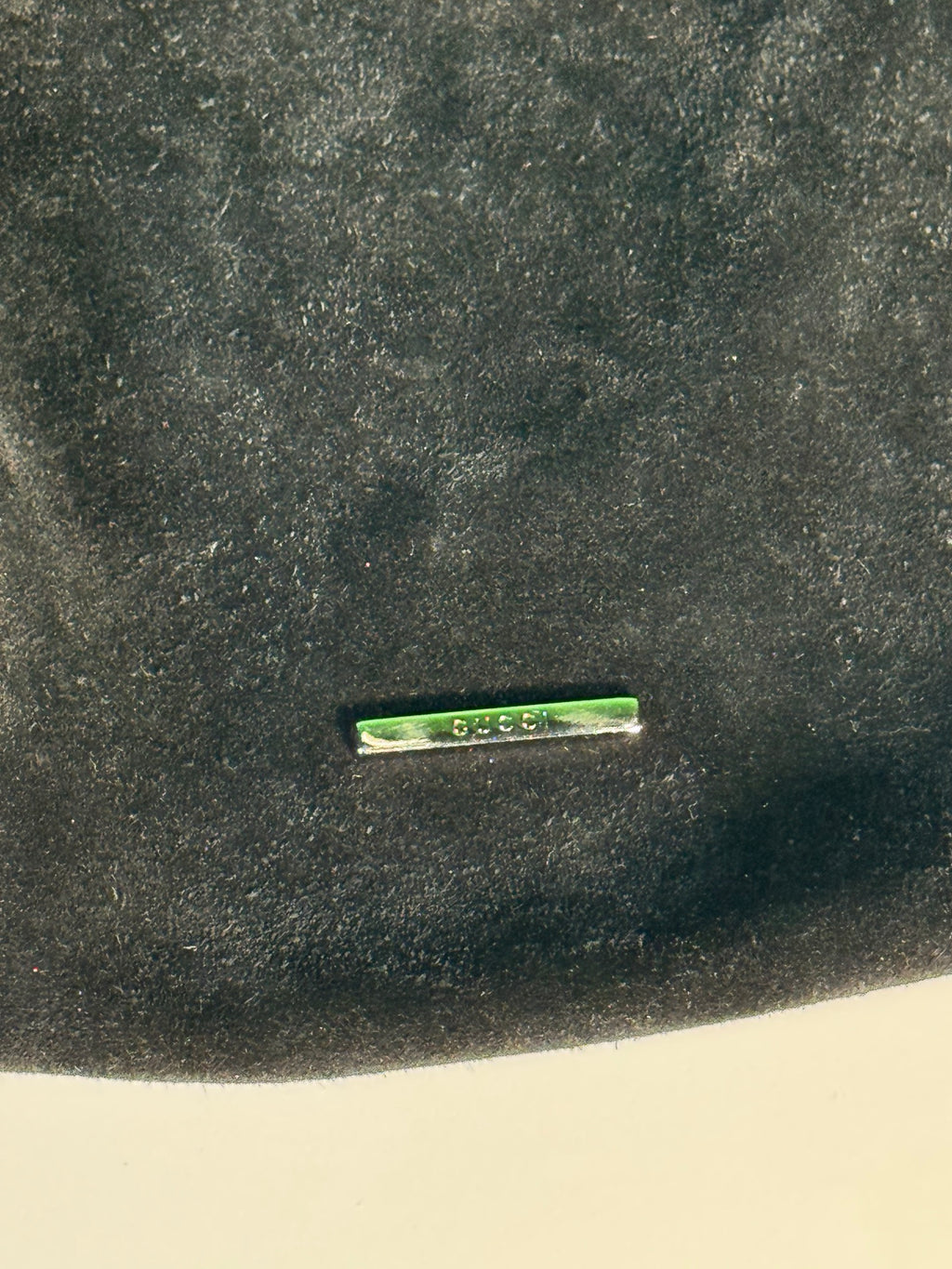 Green label or tag with 'GUCCI' text embossed on black suede exterior surface