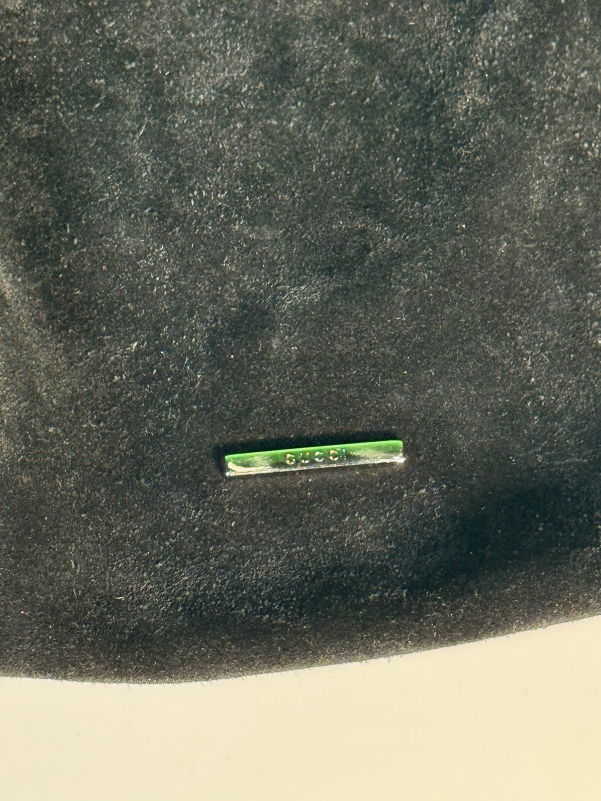 Green label or tag with 'GUCCI' text embossed on black suede exterior surface