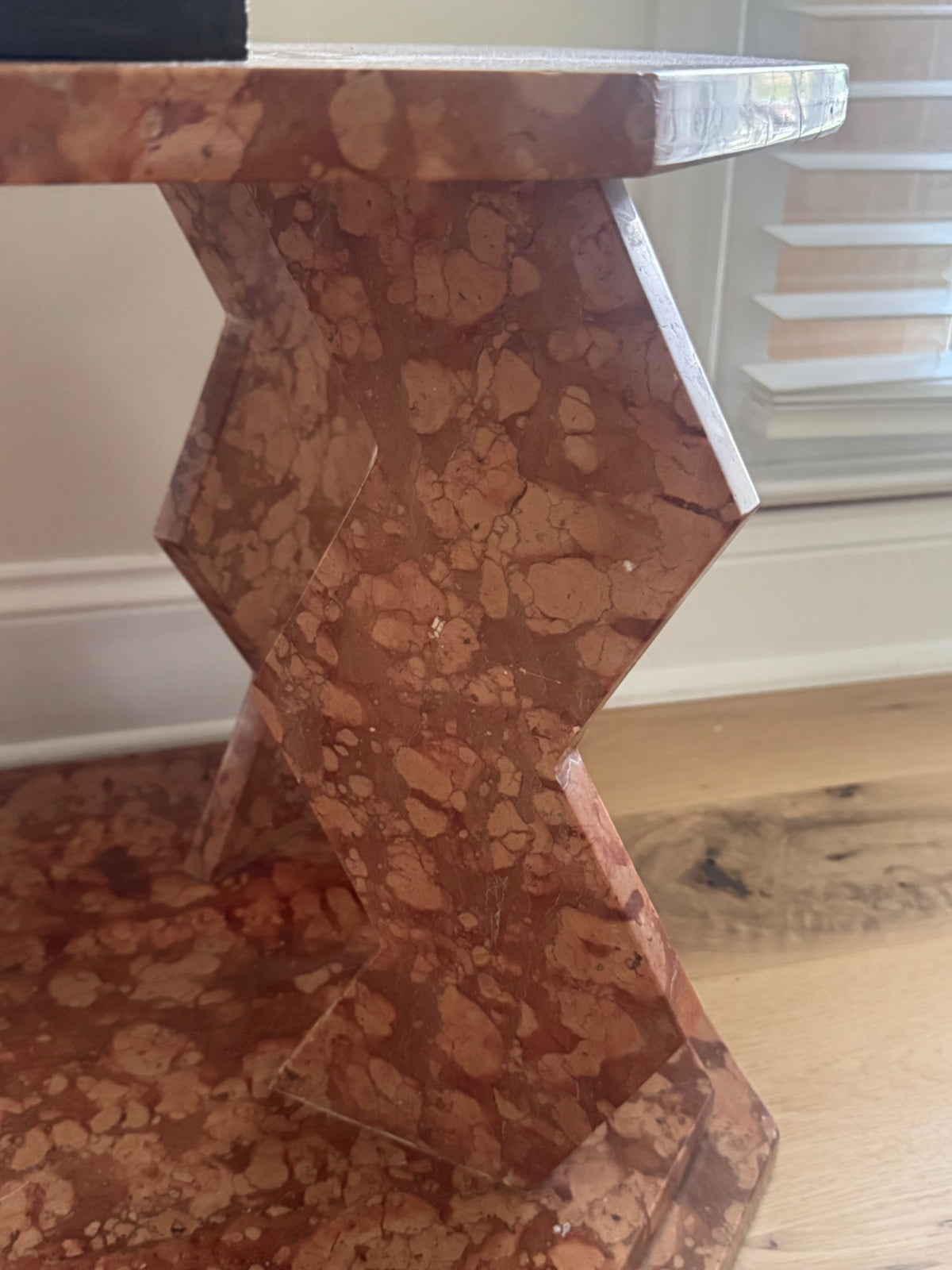 Side angle of pedestal base showing geometric zigzag form and tessellated marble surface with warm reddish-brown tones