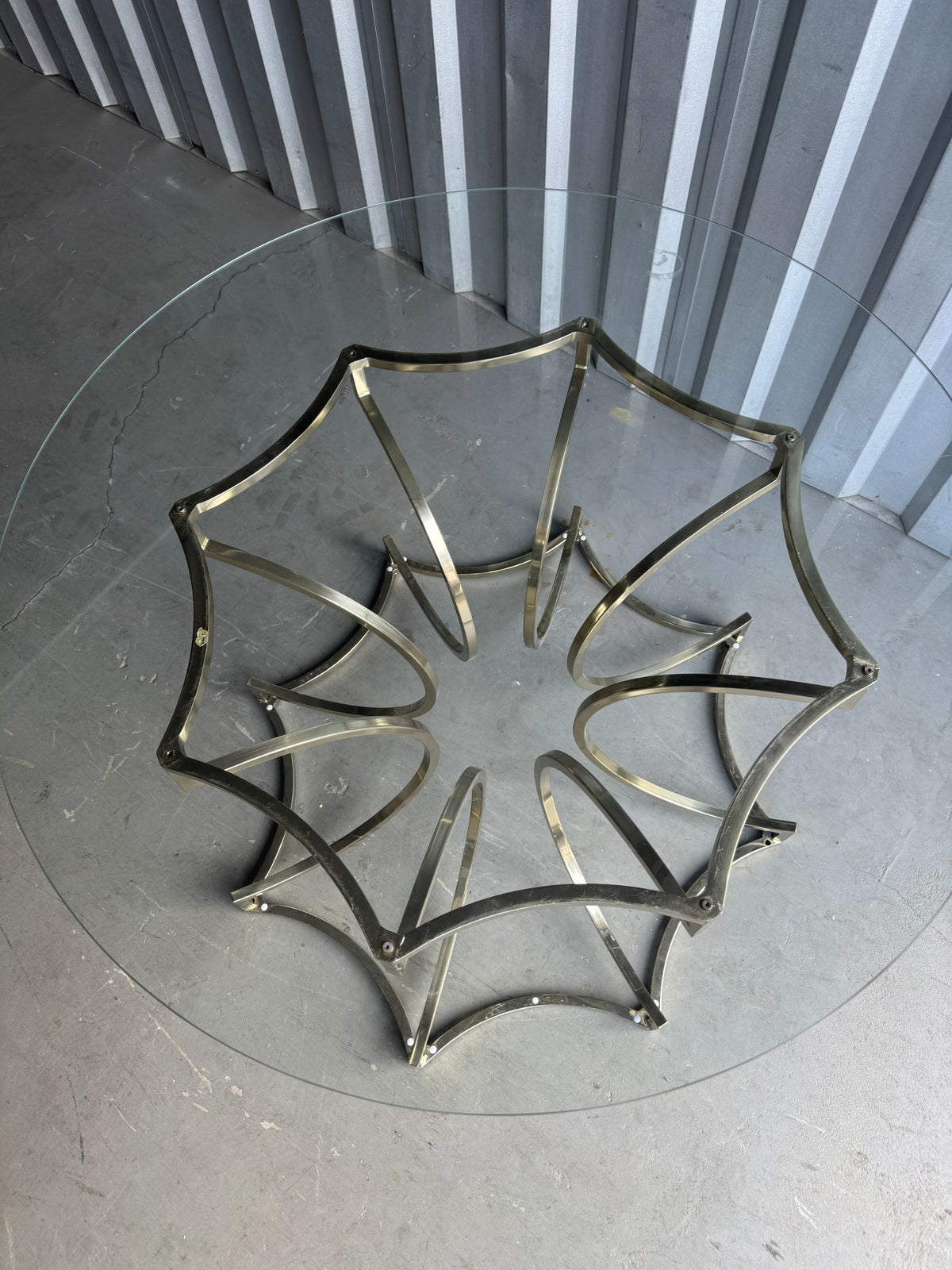 Overhead view of brass star base table on concrete floor, showing base structure and glass top from above
