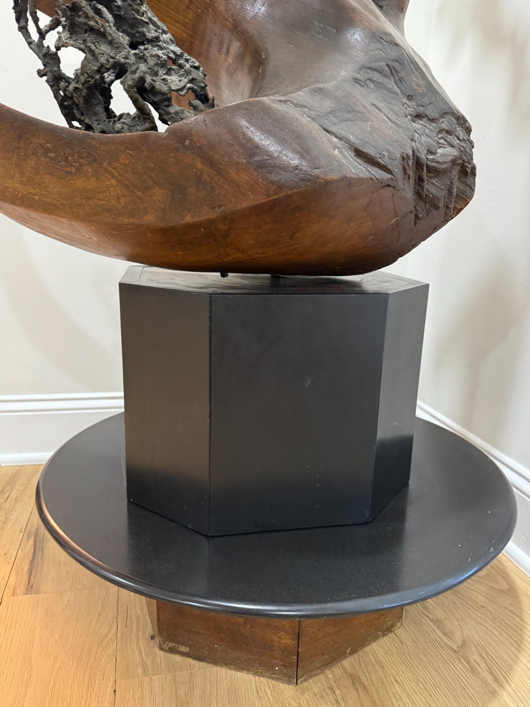 Hexagonal black base and lower section of sculpture showing carved wooden forms and dark textured material detail on interior surface