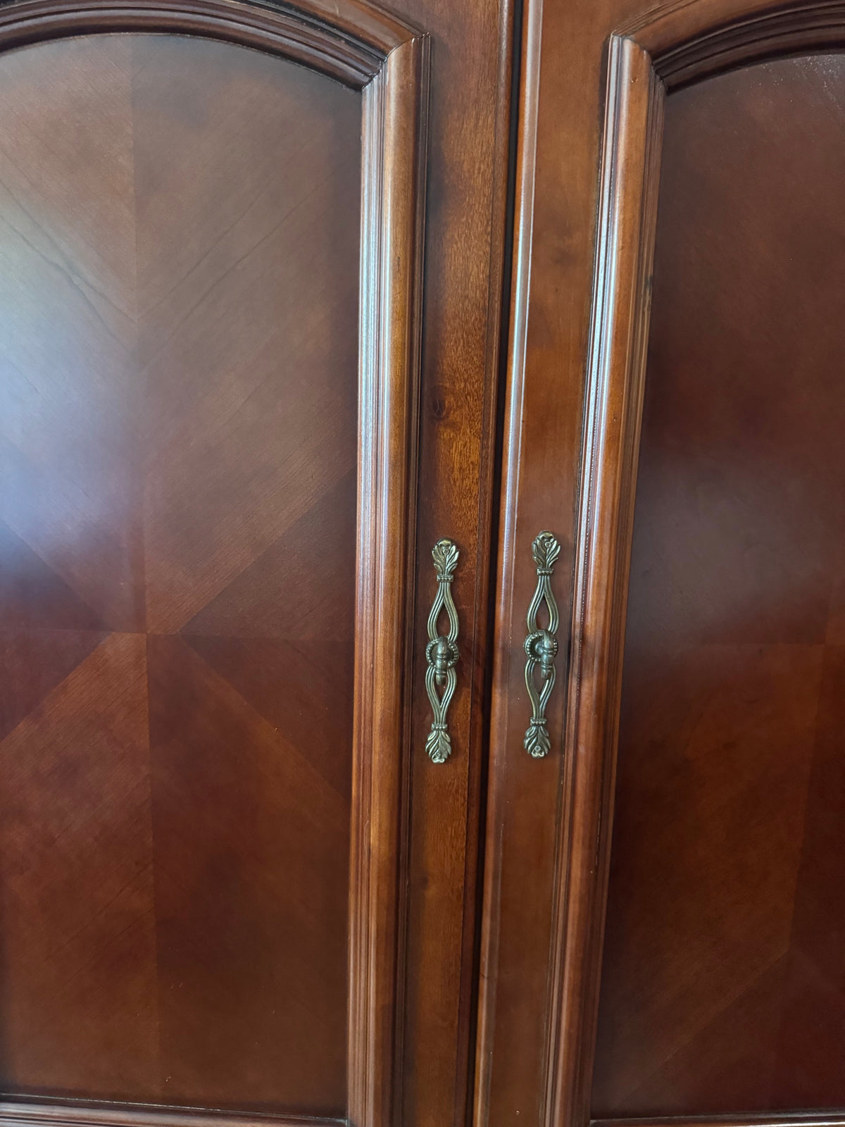 Close-up of arched door panels and brass-tone pull handles on armoire