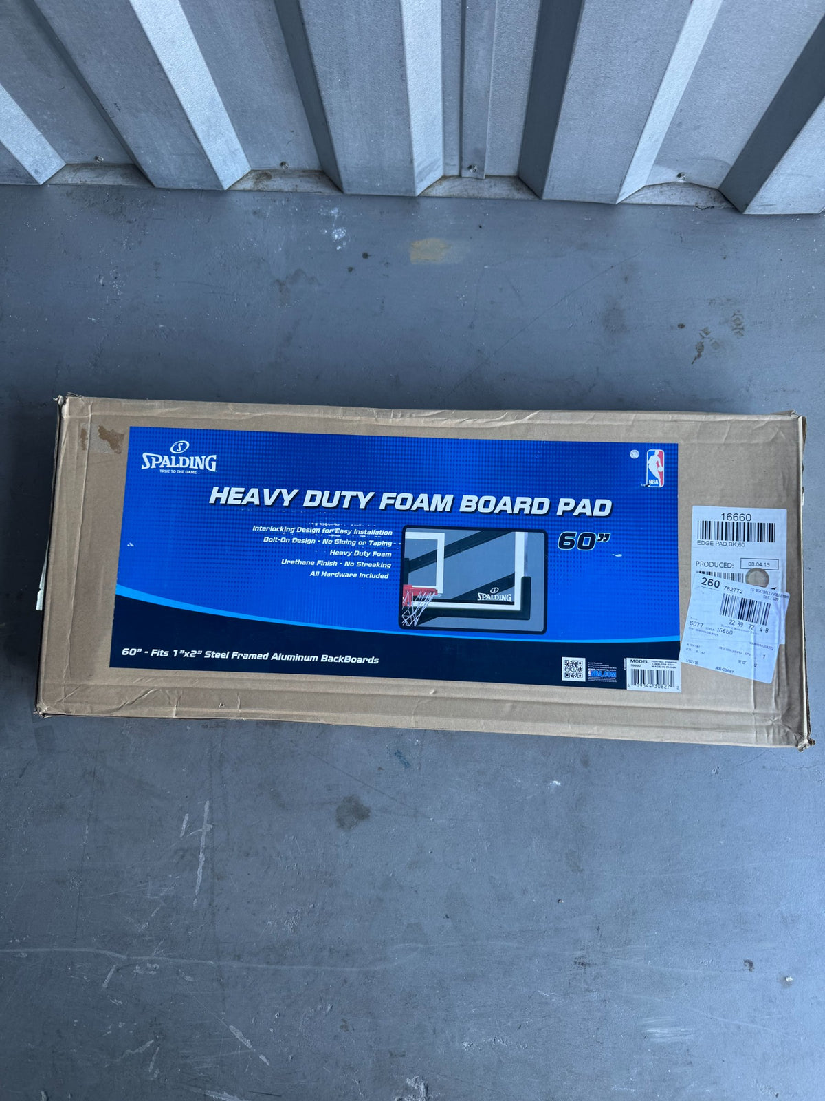 Overhead view of Spalding foam board pad boxed package on concrete surface with retail stickers and barcode labels attached to cardboard box