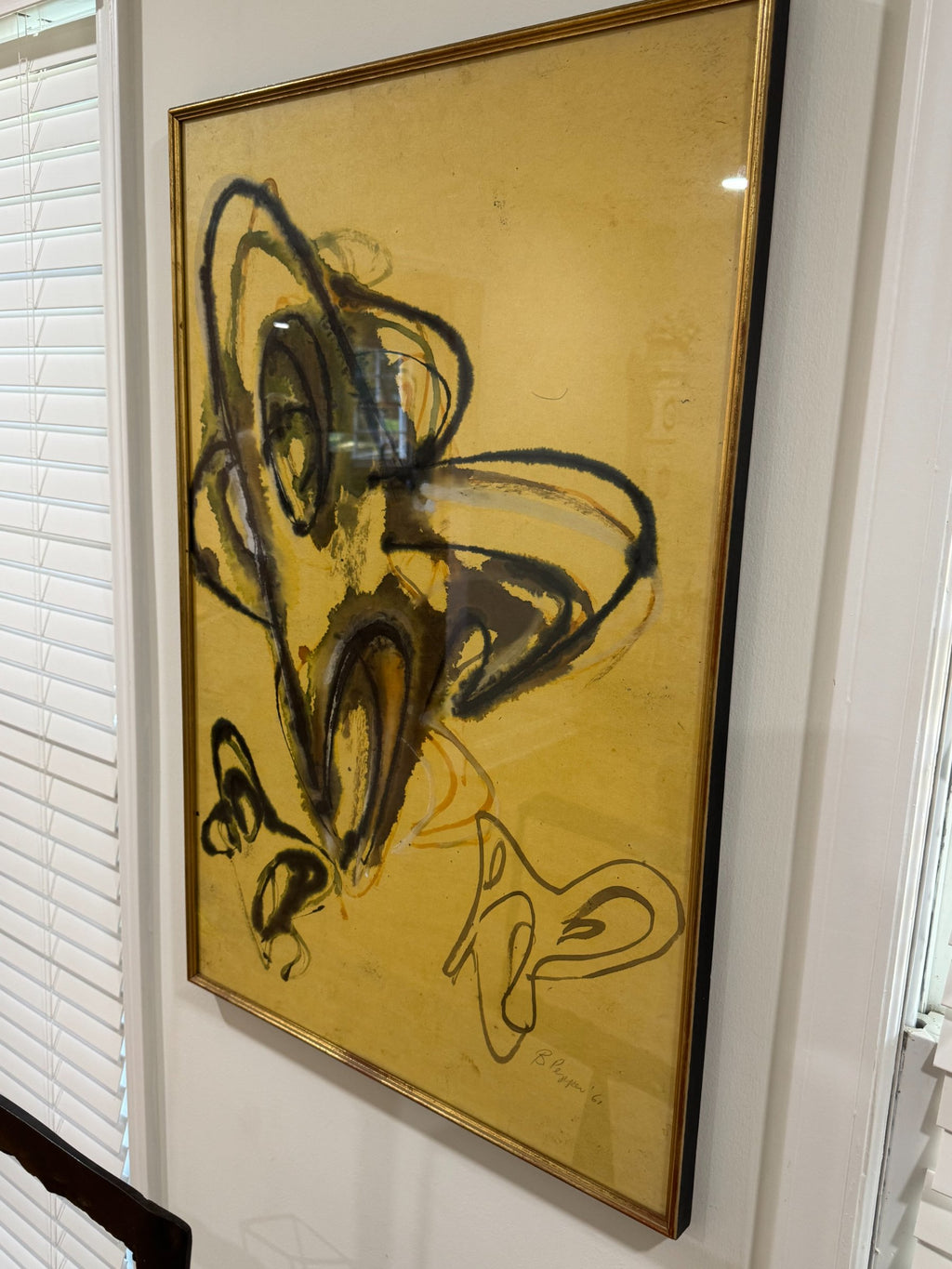 Full framed artwork on white wall, gold frame containing abstract composition with black linear elements and yellow tones