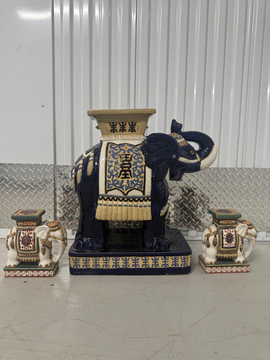 Large central cobalt blue ceramic elephant with gilt saddle cloth, flanked by two smaller cream and gold elephant stools on black base
