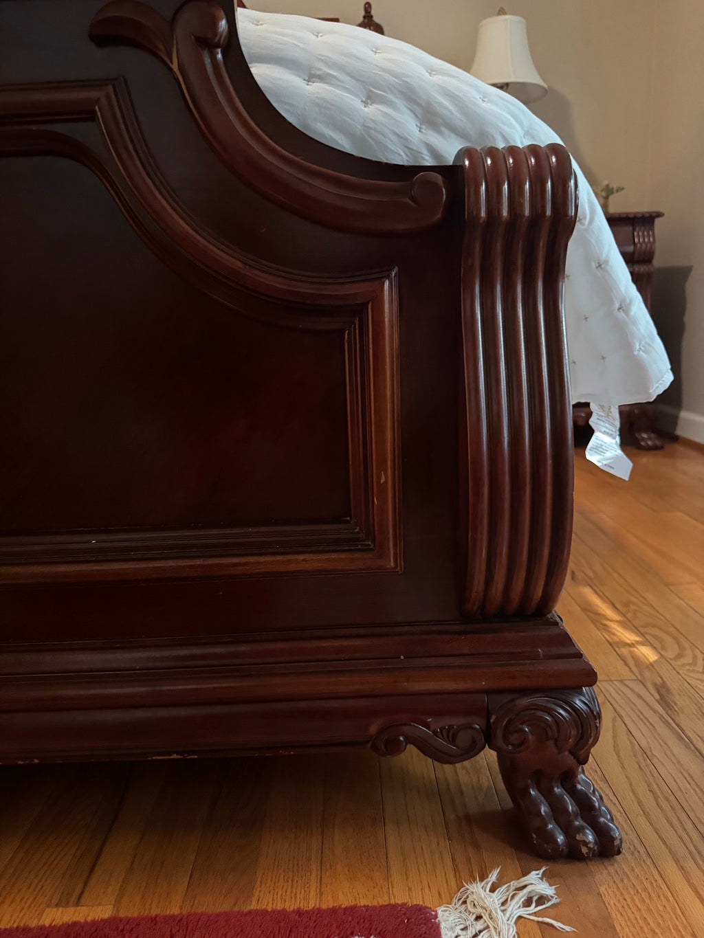 Close-up of the footboard corner showing reeded pilaster, carved scrollwork, and ball-and-claw foot