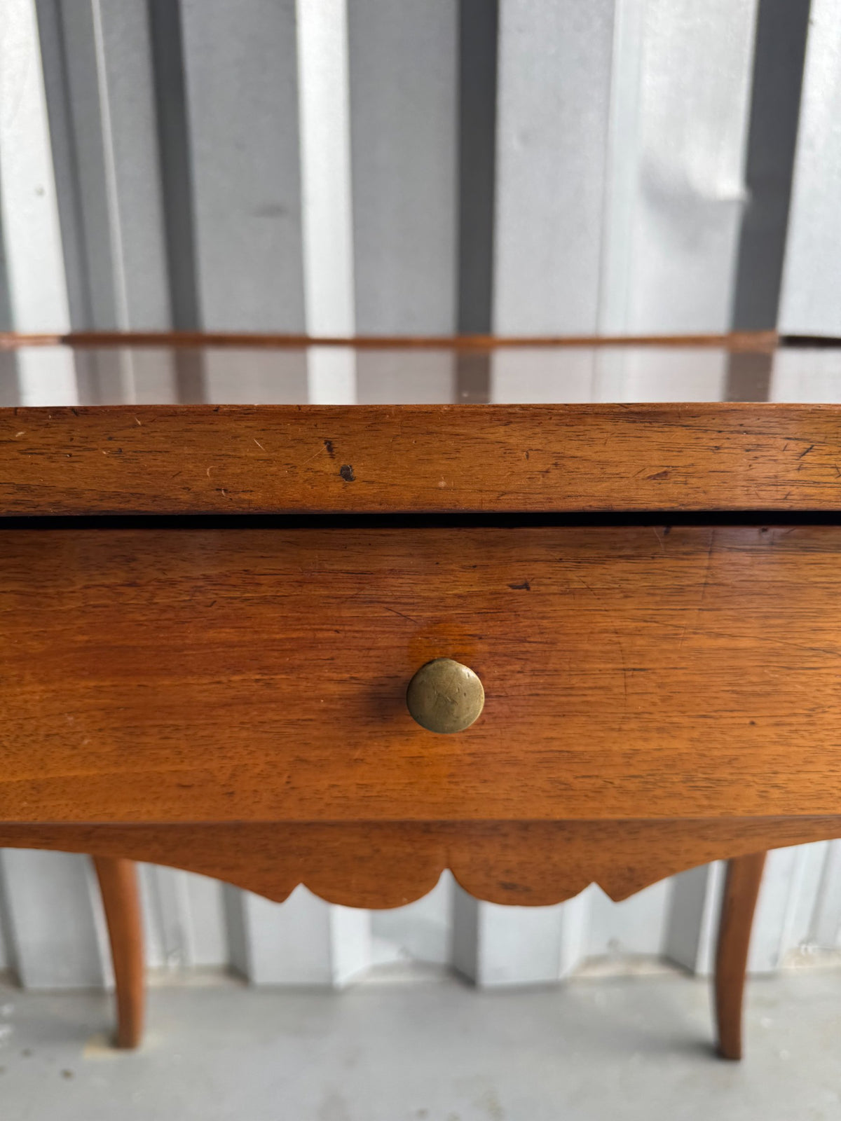 Detail of brass knob pull on front drawer of walnut table with scalloped apron below