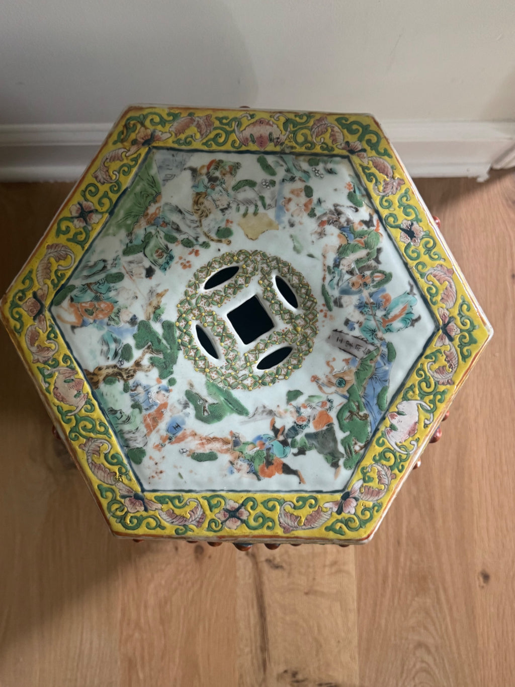 Top-down view of hexagonal stool showing yellow scrollwork border, painted figures and landscape scene, ventilation holes