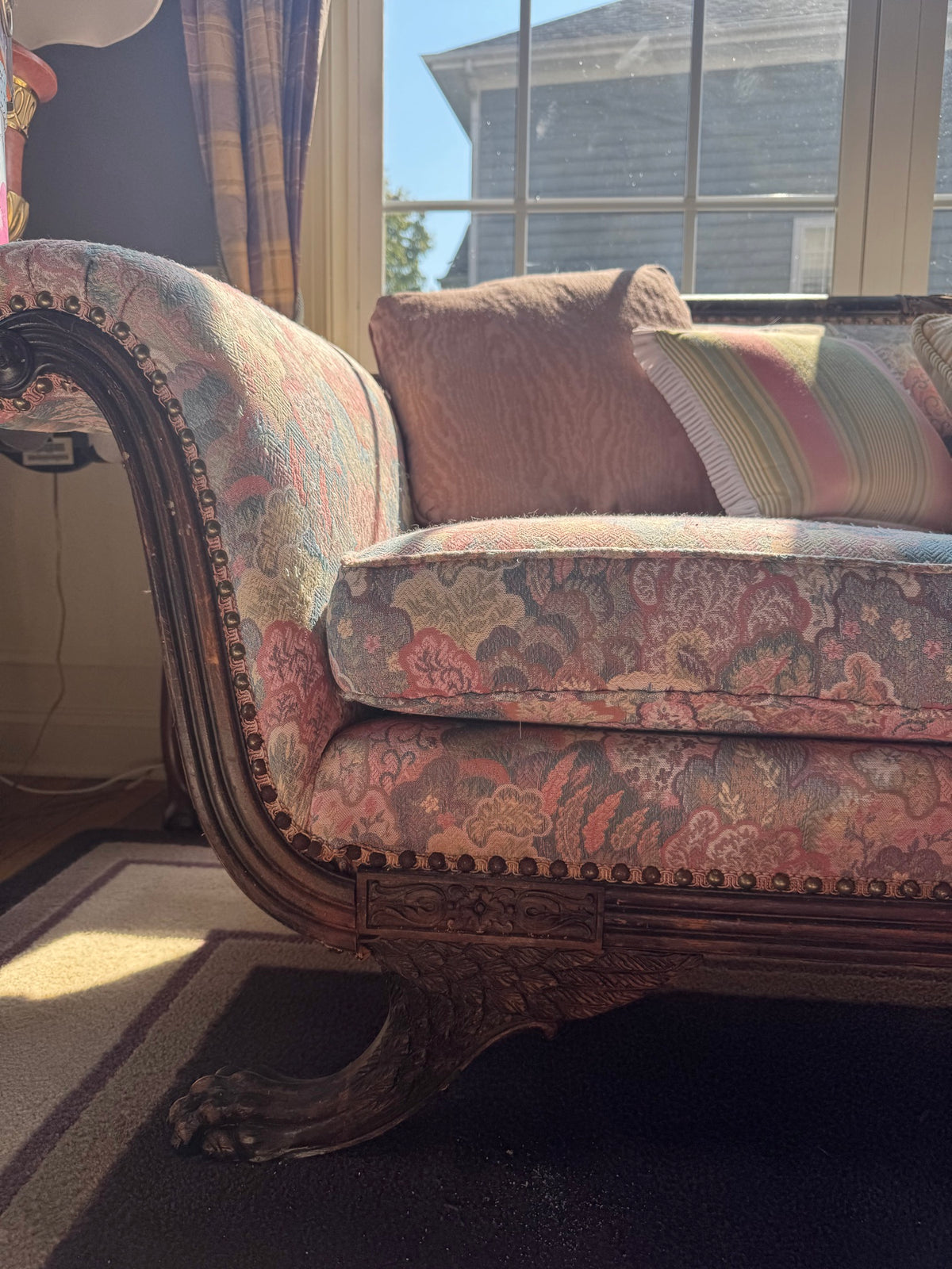 Close-up detail of left arm showing carved wooden frame, damask fabric in red and cream tones, and decorative nailhead trim
