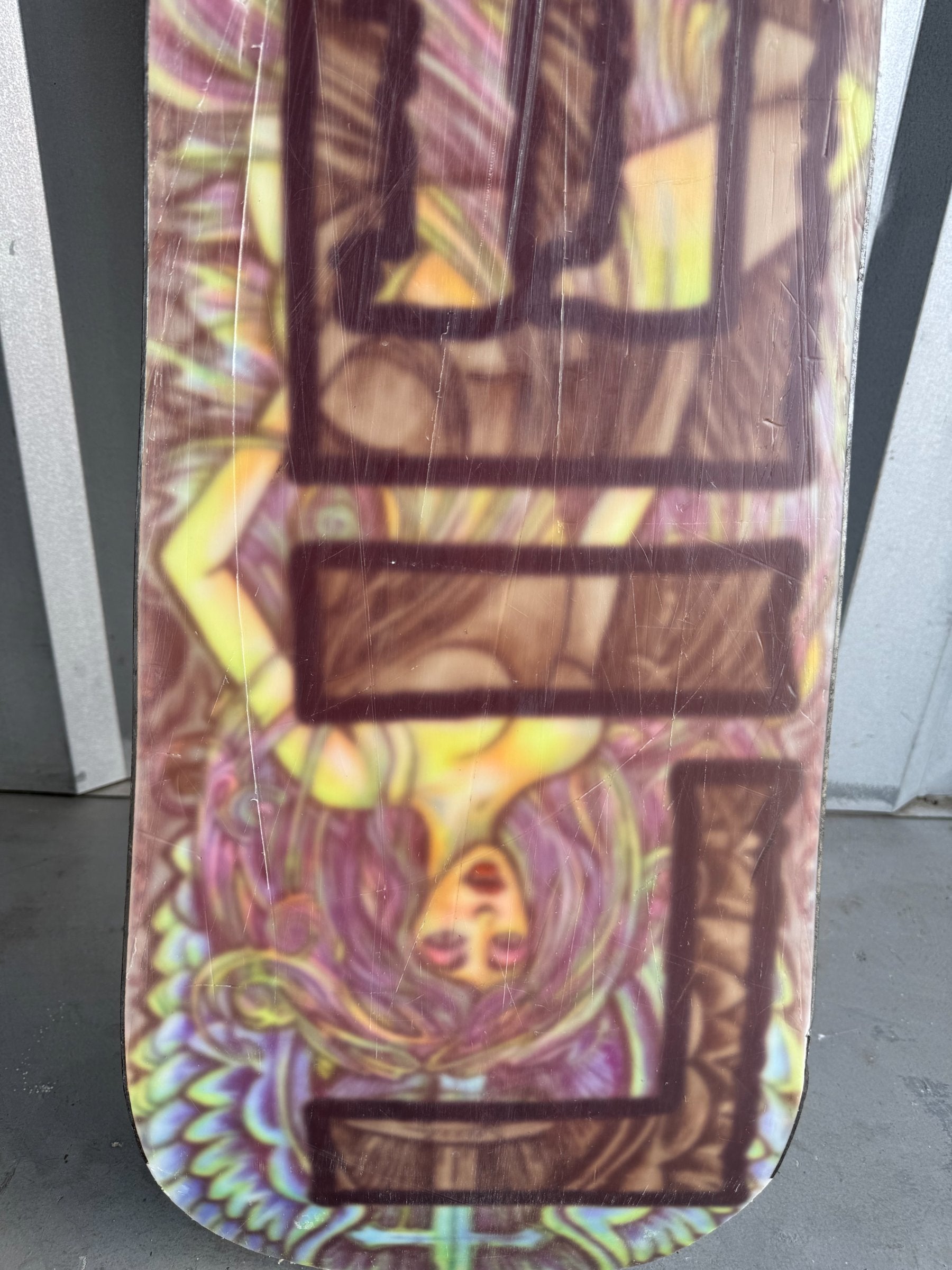 Close-up of snowboard mid-section showing brown rectangular branding elements and yellow decorative patterns on colored background