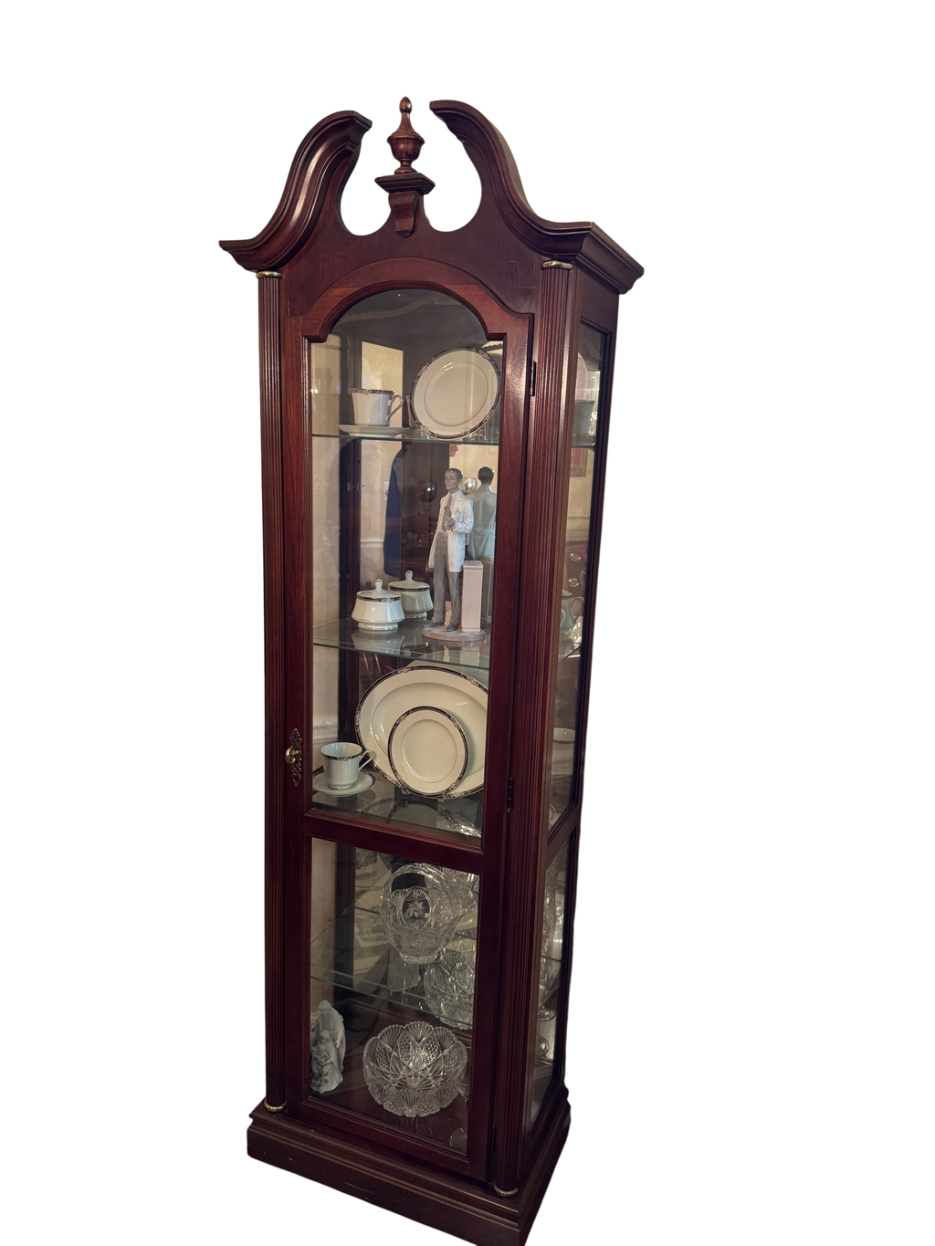 Tall mahogany finish display cabinet with broken pediment top, arched glass door, and glass shelves holding china and crystal.