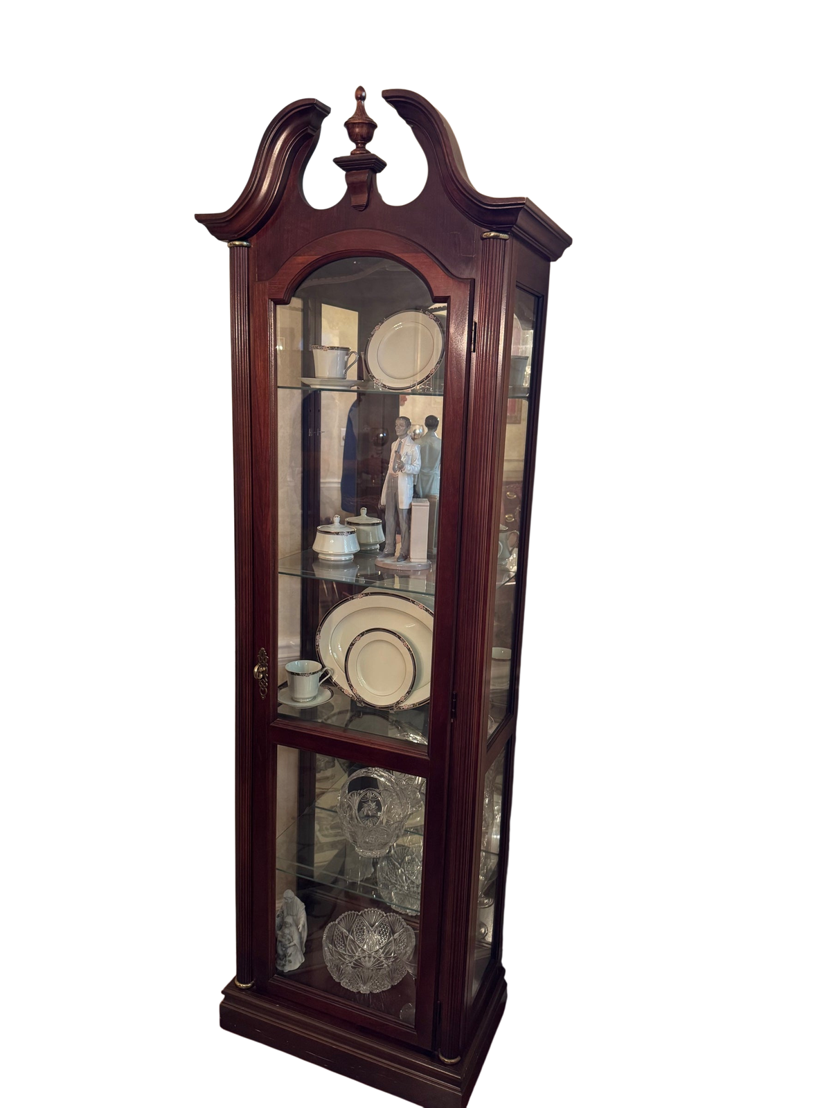 Tall mahogany finish display cabinet with broken pediment top, arched glass door, and glass shelves holding china and crystal.