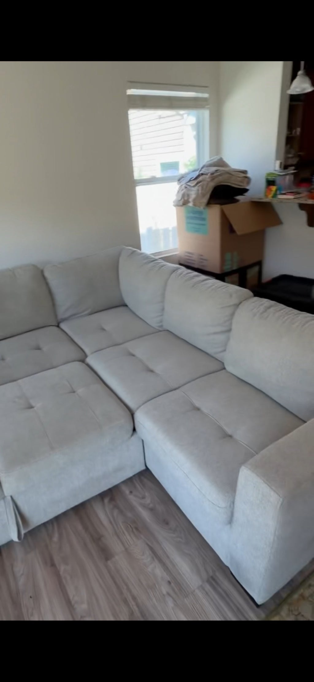 Gray modular sectional sofa with chaise lounge in bright living room with window and moving box