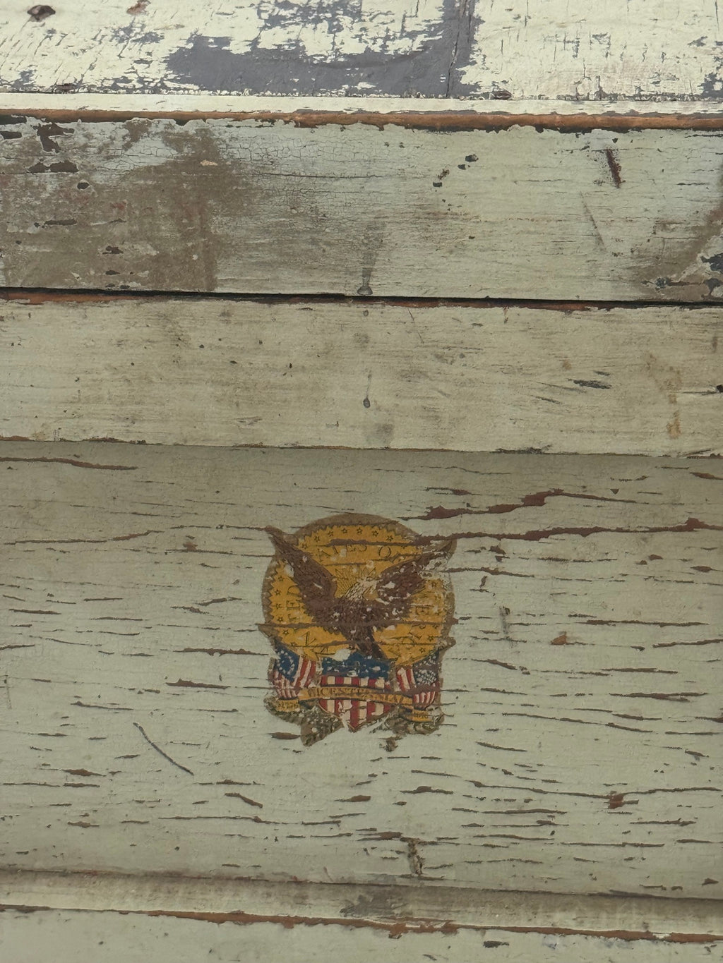 Single gold eagle decal with shield and stars, centered on cream painted wooden panel with visible wear and distressing