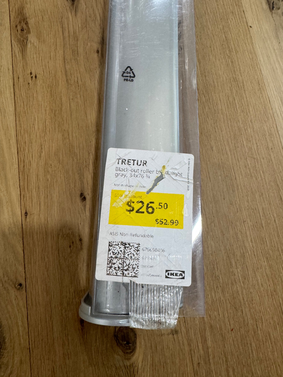 Close-up of IKEA TRETUR roller blind label on wooden floor, gray fabric visible, price tag and product details legible