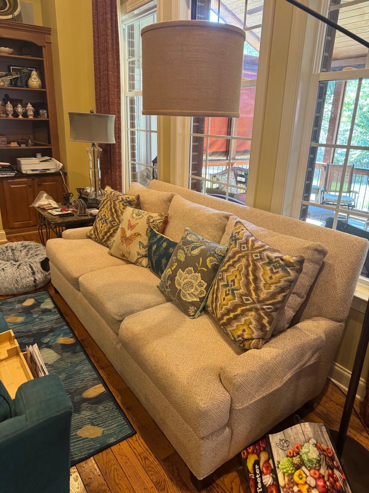 Side angle of upholstered armchair with oatmeal fabric, rolled arm detail, and matching patterned throw pillows in warm earth tones