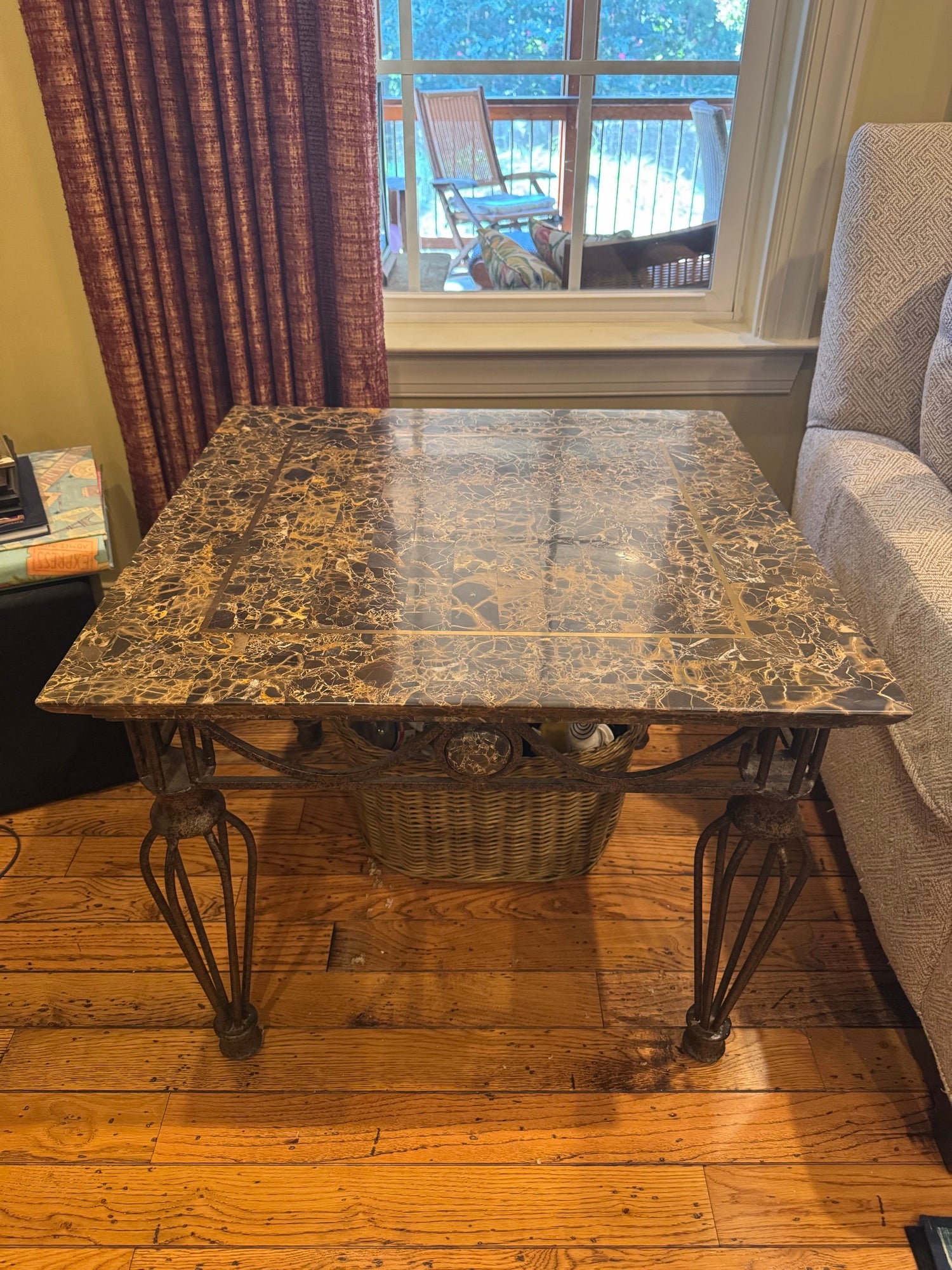 Full view of marble top occasional table with ornate iron legs and woven basket shelf, positioned in room with hardwood floor
