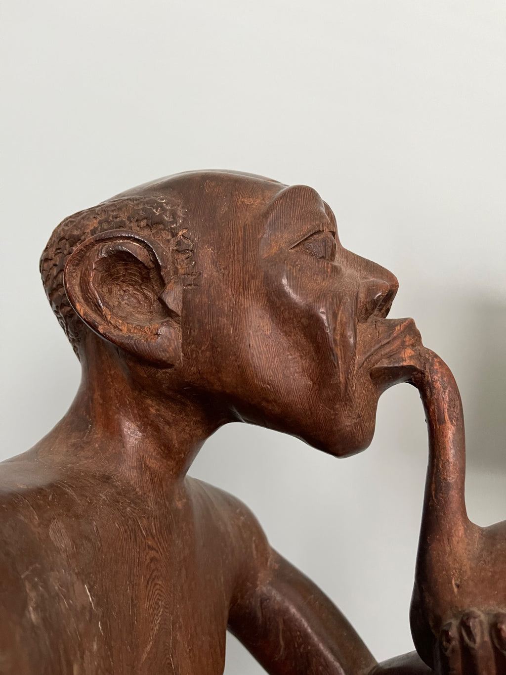 Profile view of carved wooden figure showing side of face, pointed chin, hand raised to horn