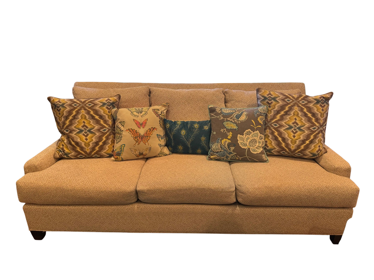 Front view of three-cushion sofa with oatmeal textured upholstery, rolled arms, and decorative patterned pillows in gold and jewel tones