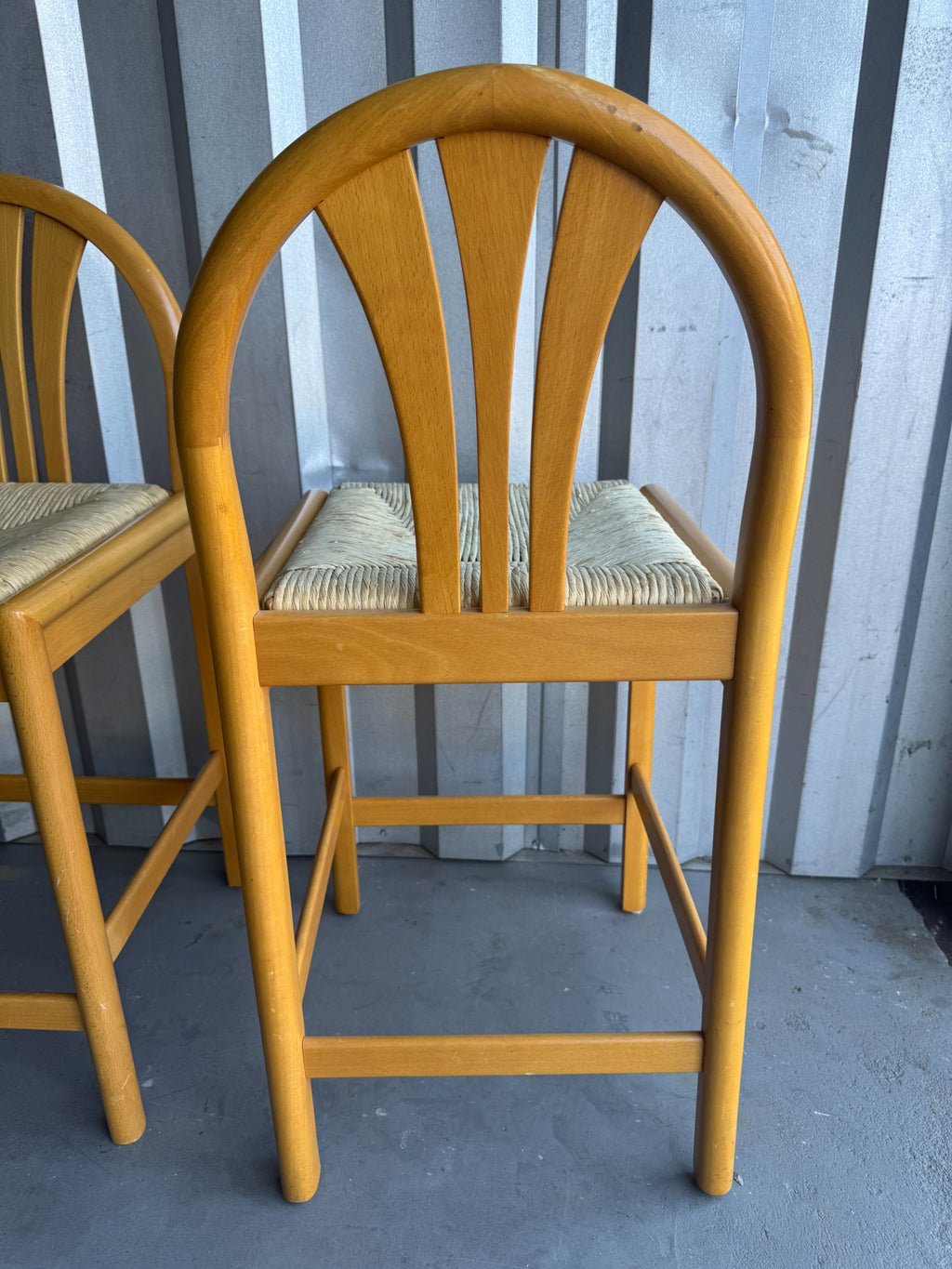 Single bar stool from side angle displaying curved wooden backrest with vertical slats and rush seat