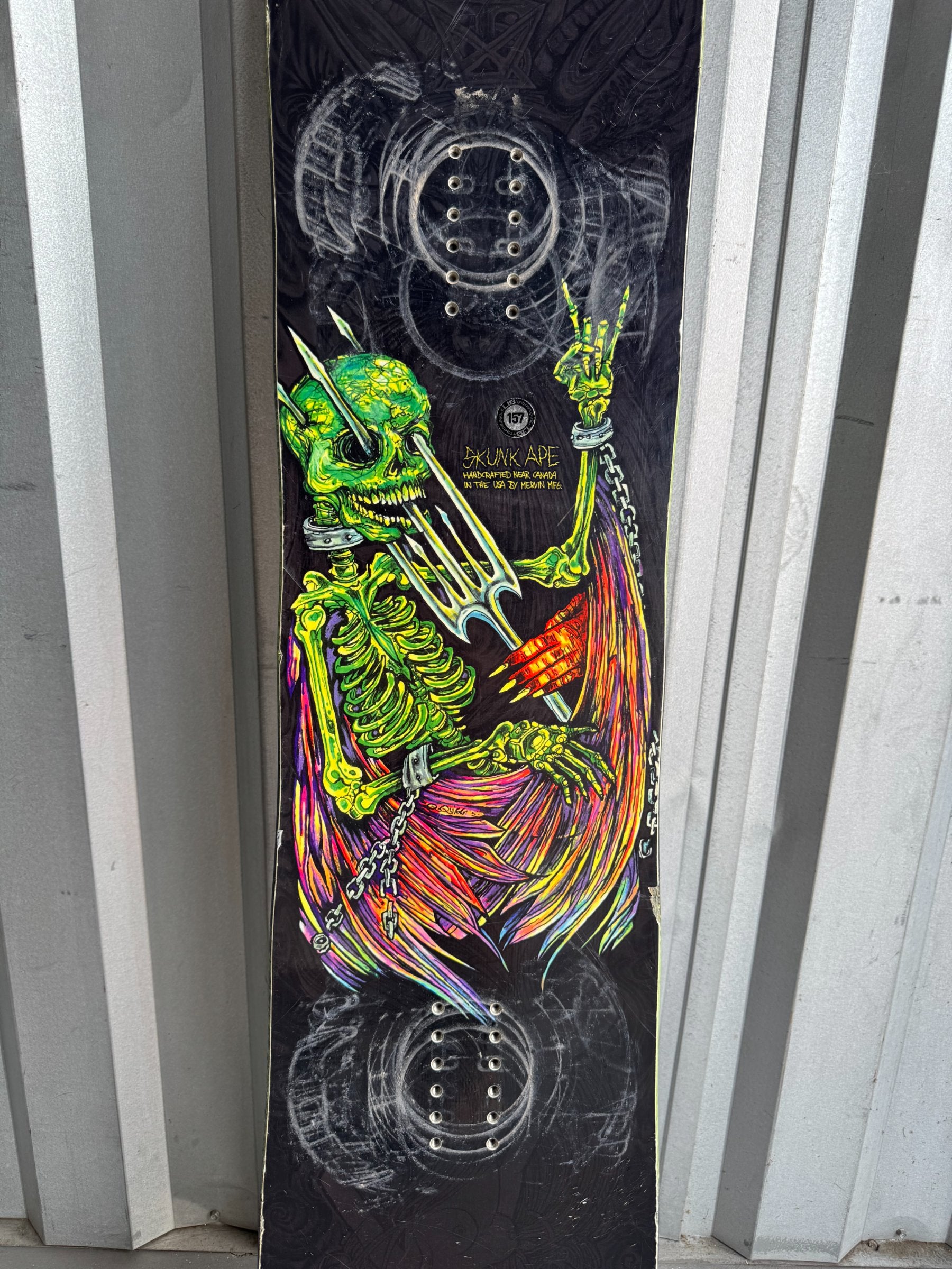 Full snowboard length displayed against corrugated backdrop, black base with complete skeleton graphic from top to bottom