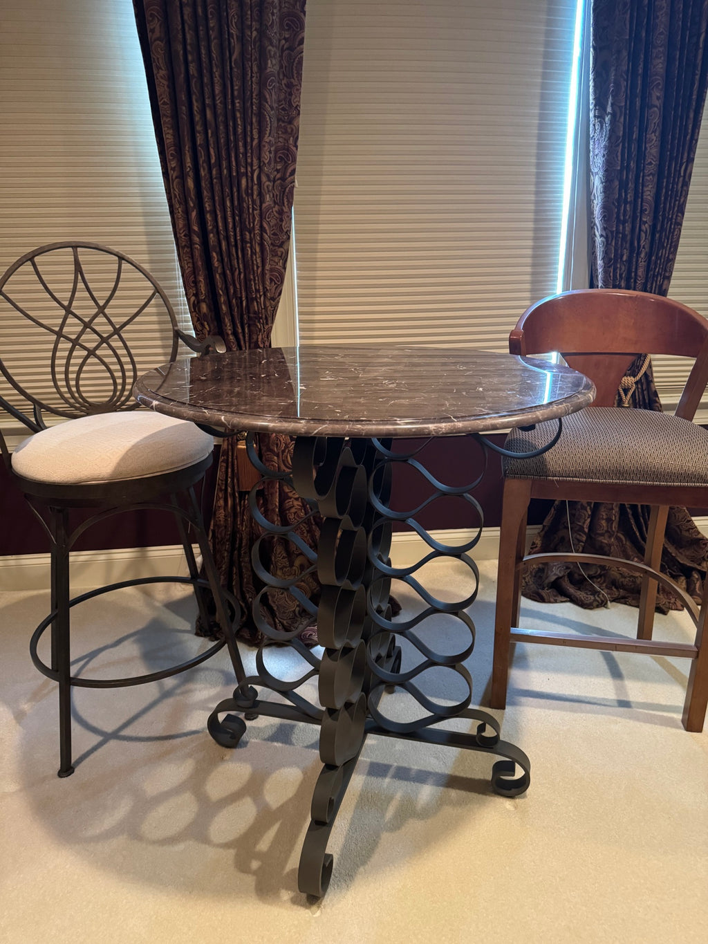 Round marble-top pub table with ornate scrolled iron pedestal base, viewed from above with two matching stools