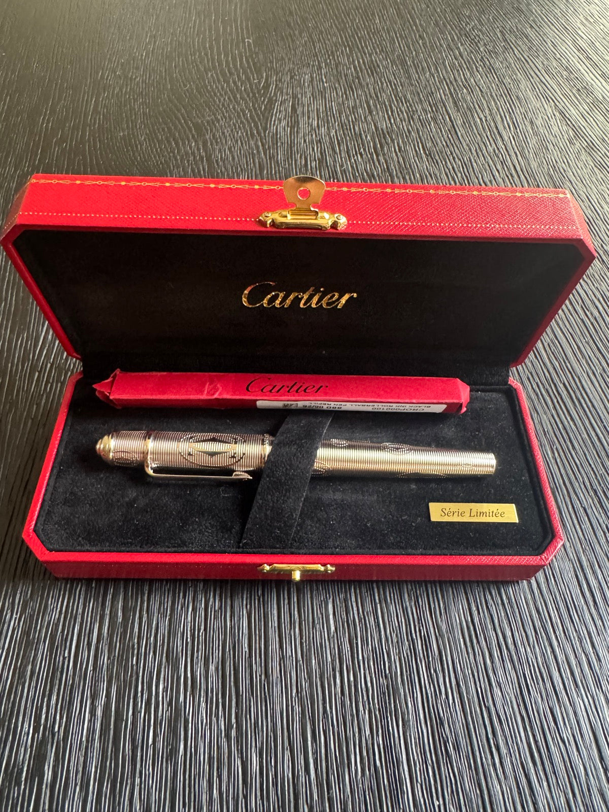 Open Cartier box interior showing black velvet lining, gold-toned rollerball pen, and red Cartier refill packet
