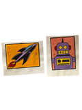Pair of hand-colored linocuts, rocket and robot, side by side on a grey cloth