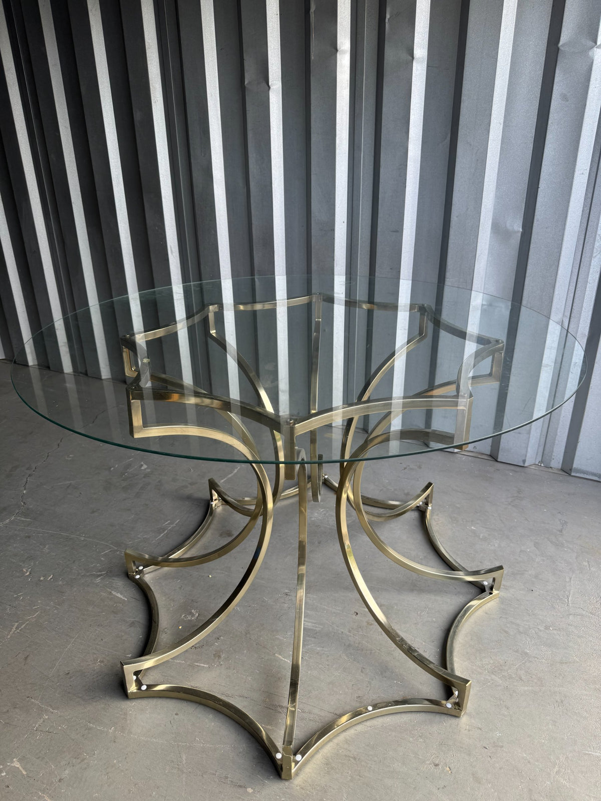 Side view of brass star base table against striped backdrop, showing curved brass legs and round glass top