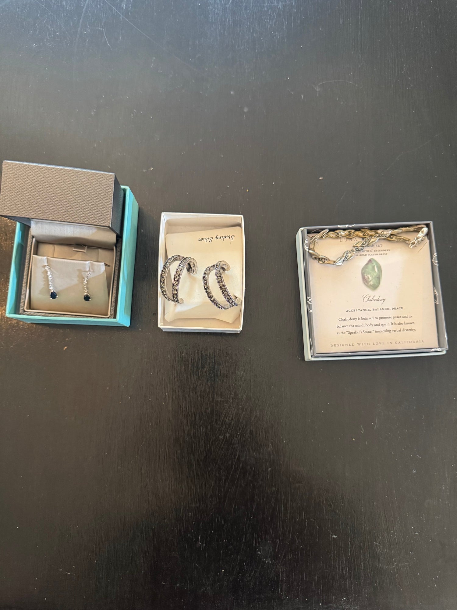 Three separate jewelry items displayed: drop earrings with dark stones, curved marcasite hoop earrings, and packaged chalcedony bracelet set