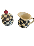 Black and white checkered sugar bowl with lid topped by red finial, and matching cream pitcher displayed on dark wood surface