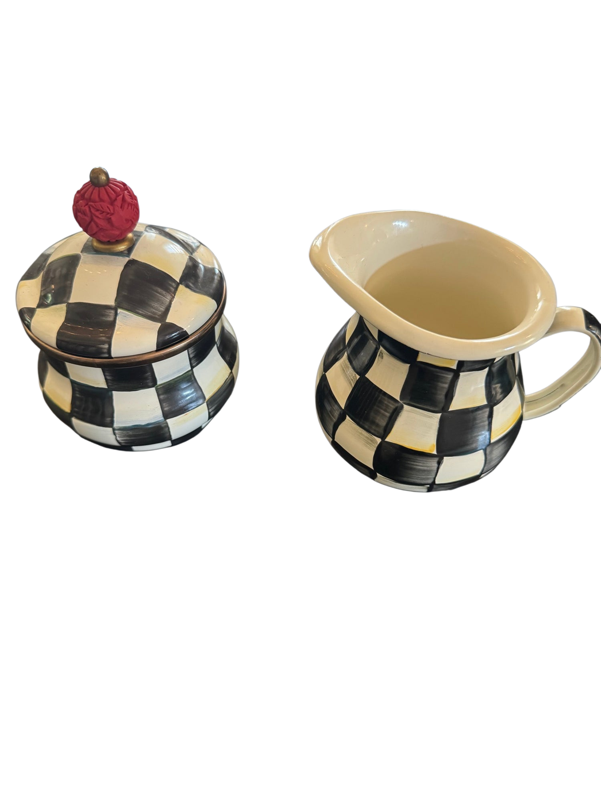 Black and white checkered sugar bowl with lid topped by red finial, and matching cream pitcher displayed on dark wood surface