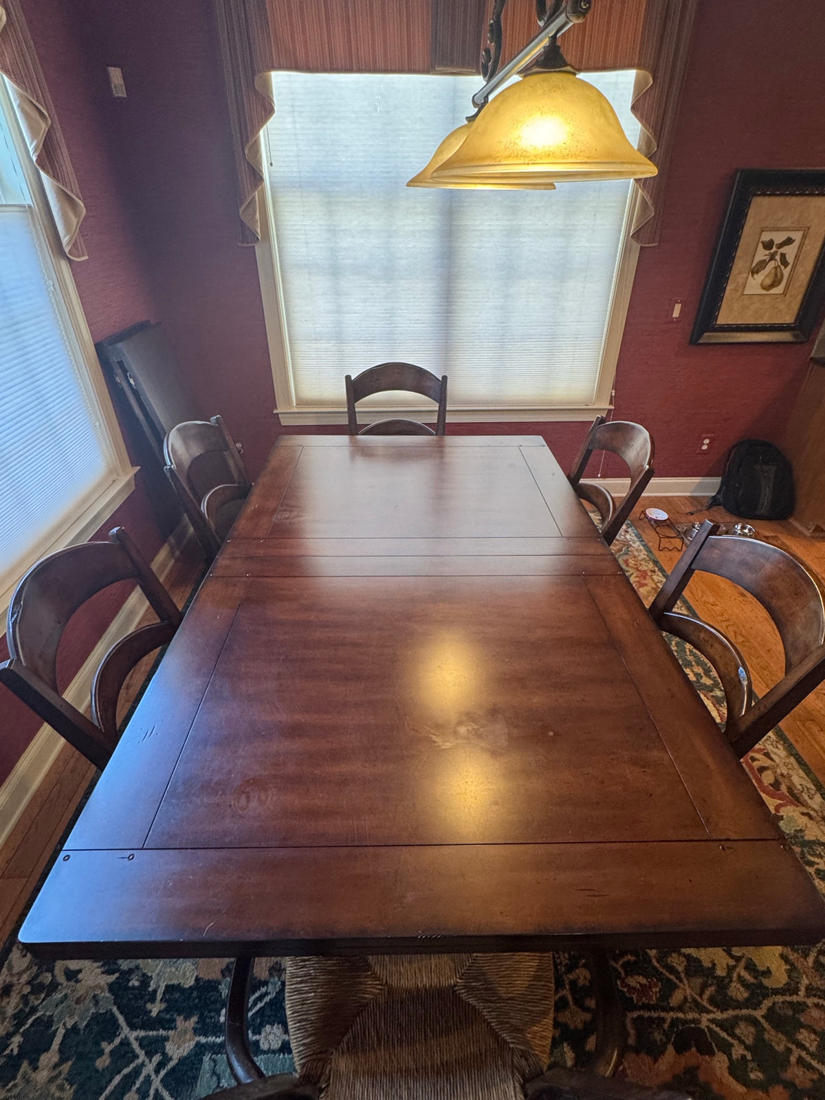 Extended dining table from end view showing full length with leaf extensions, four chairs visible, gold pendant light