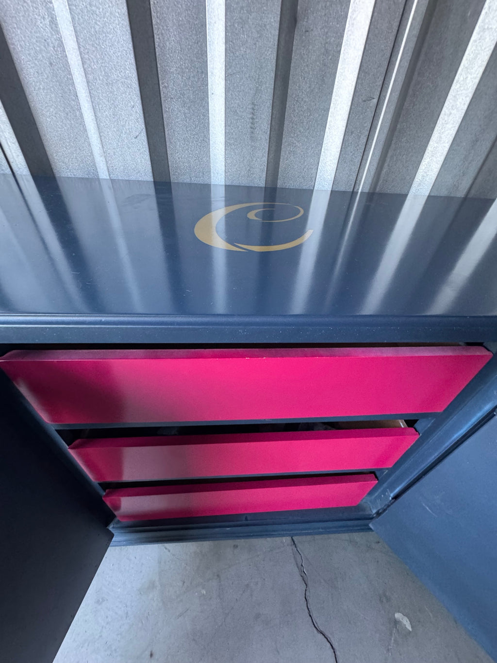 Navy blue credenza with pink/magenta drawer fronts and gold monogram logo, viewed from above at an angle