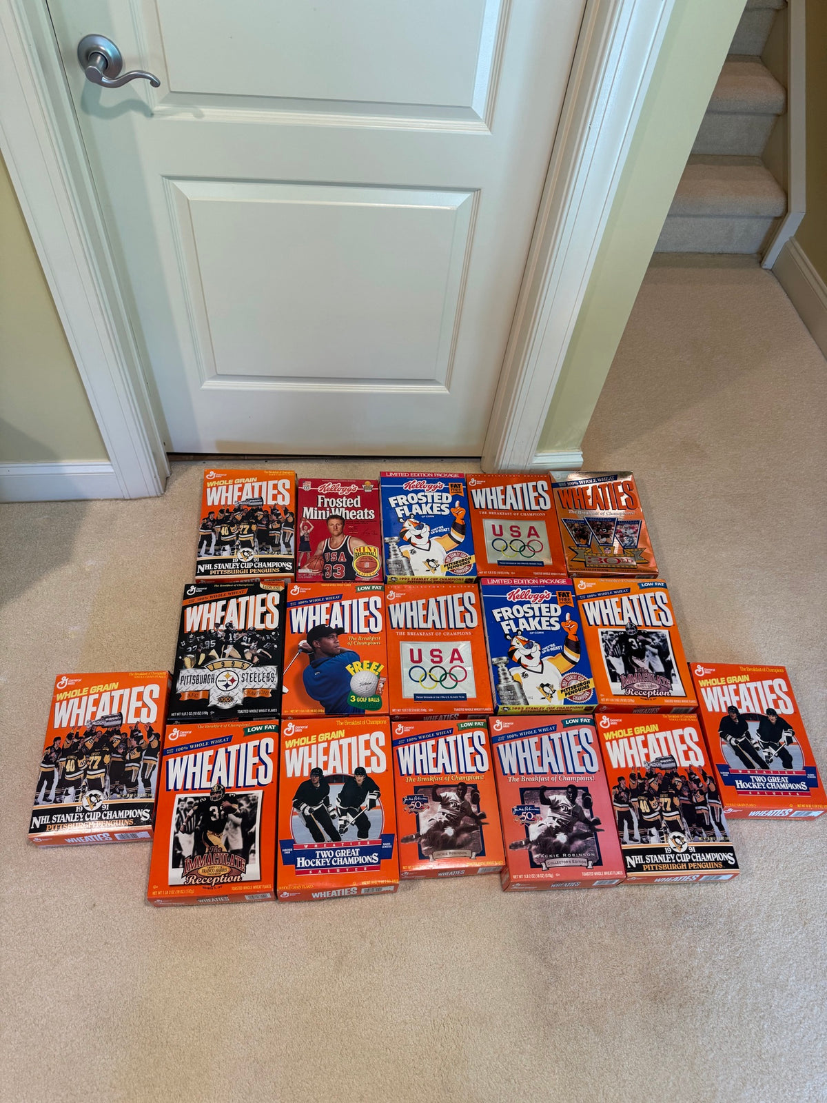 Collection of approximately twenty unopened cereal boxes arranged on carpeted floor, showing Wheaties and Frosted Flakes with various sports imagery
