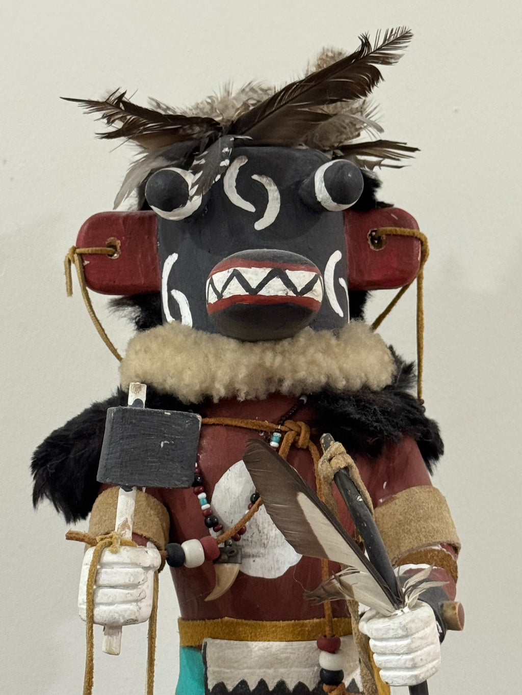 Frontal view of face mask with white crescent moon designs, geometric mouth pattern, and feathered crown arrangement