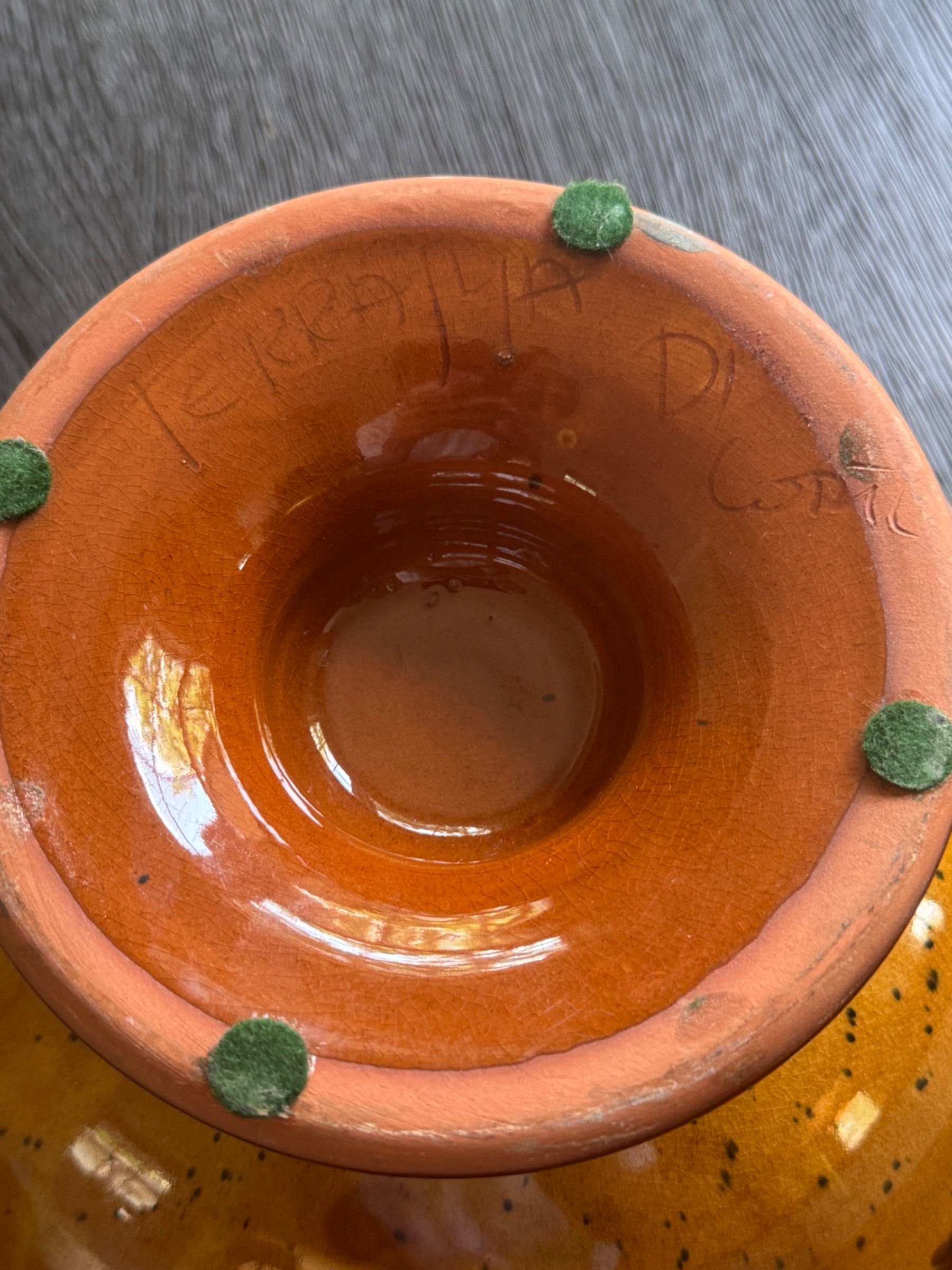 Interior view of terracotta bowl showing unglazed orange-red clay body with green felt protective pads on rim