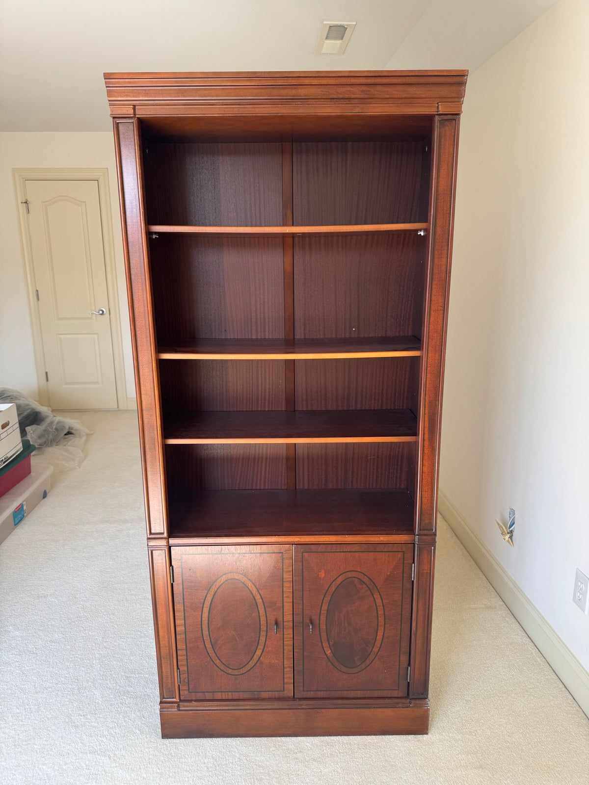 Mahogany bookcase with decorative oval inlaid panels on cabinet doors, open shelving above, front facing view