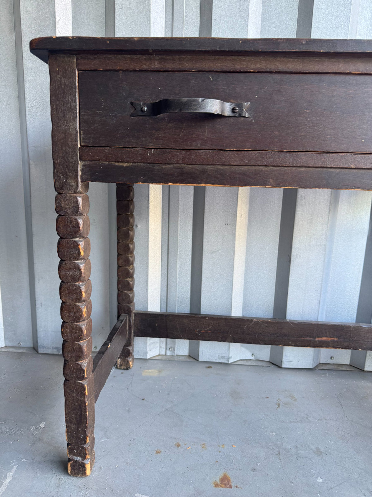 Close-up of drawer front showing wrought iron handle detail, dark wood finish with wear marks
