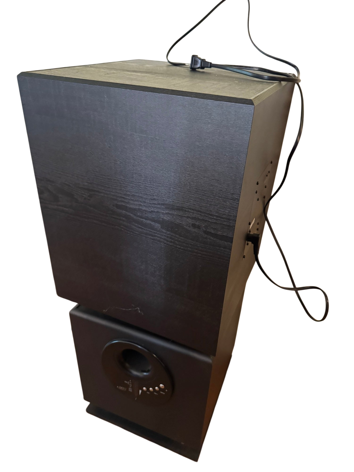Black subwoofer with textured finish, standing upright on wooden floor against cream wall