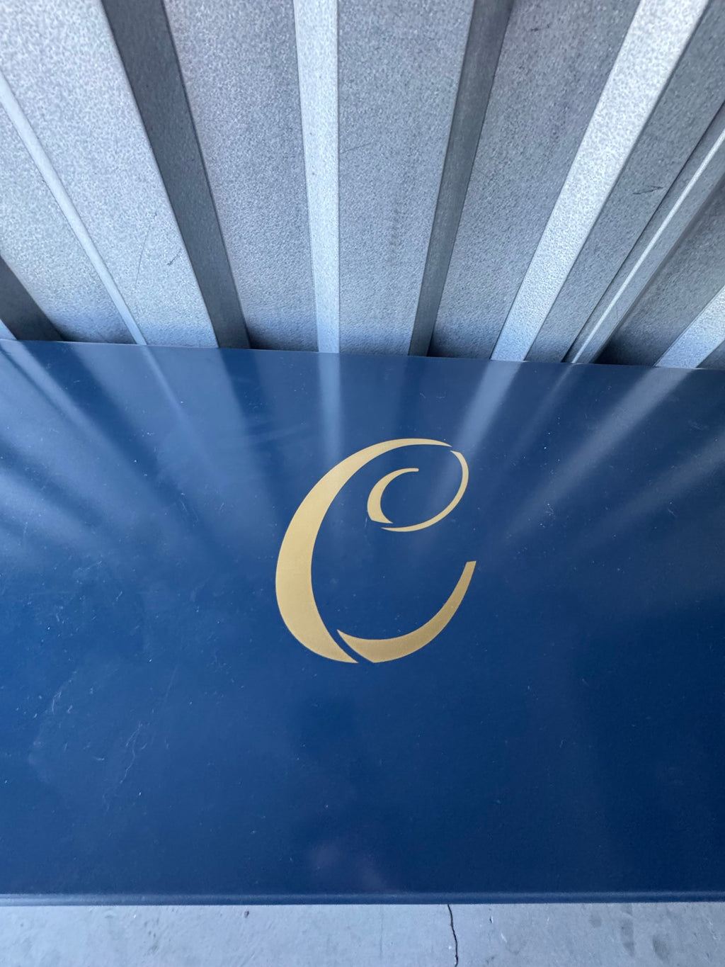 Navy blue panel with gold cursive 'C' monogram and radiating lines detail, viewed from above