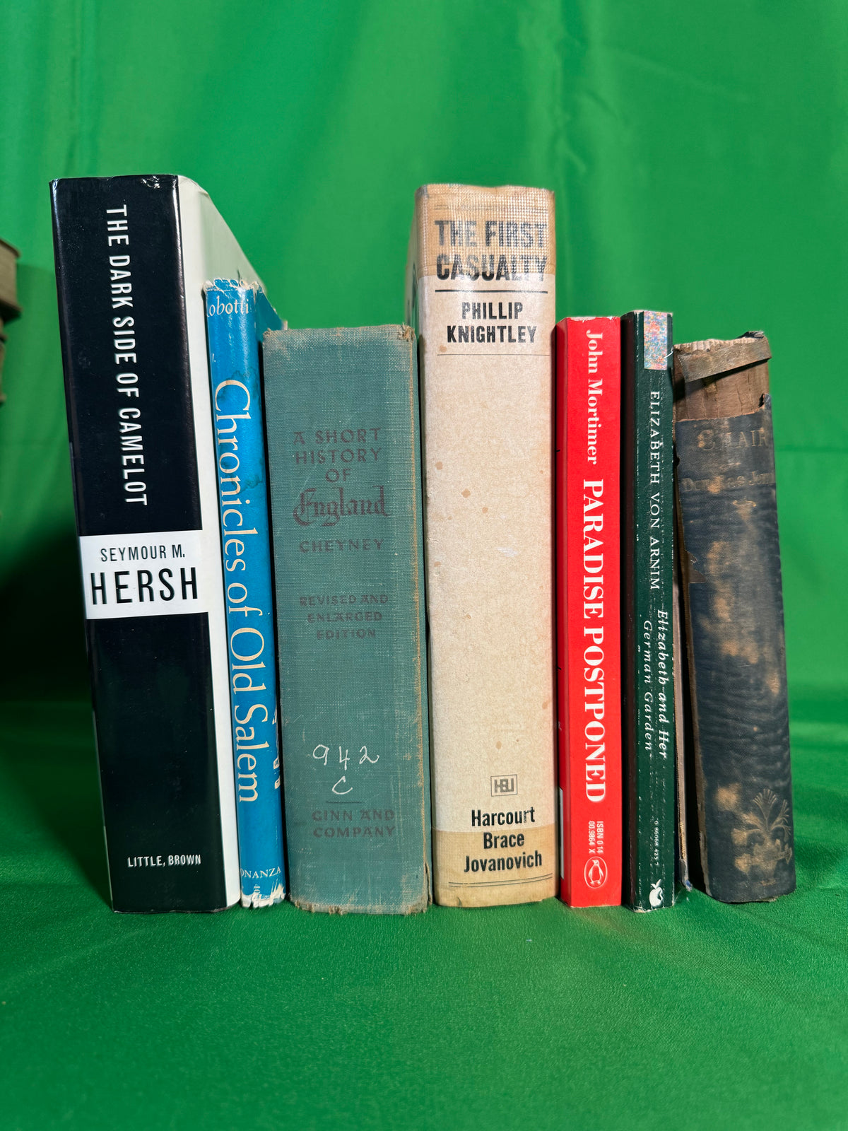Books stood spine-out on green cloth, including The Dark Side of Camelot by Seymour M. Hersh, The First Casualty by Phillip Knightley, A Short History of England and Chronicles of Old Salem